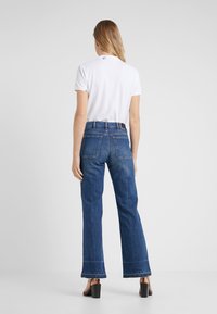 White polo shirt with short sleeves, paired with high-waisted dark blue denim flared pants featuring frayed hems and back pockets.