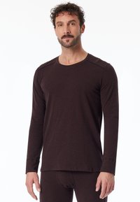 Ruskea pitkähihainen t-paita, joka on pehmeää materiaalia, pyöreällä kaula-aukolla ja hieman teksturoidulla pinnalla, joissa on kontrastivärit olkapäissä.