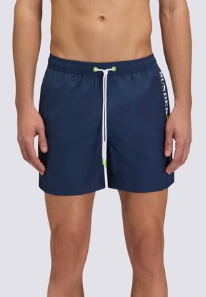 Torace maschile con indosso pantaloncini da bagno blu navy con coulisse bianca e logo "SUNDEK" sul lato destro.