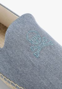Blå slip-on sko med herringbone mønster og en broderet dødningehoved og kors på aqua. Har vævet jute-detaljer rundt om sålen.