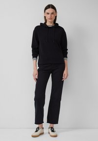 Felpa nera con cappuccio e coulisse, abbinata a jeans neri e sneakers crema con lacci neri e suole in gomma.