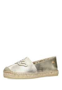 Alpargatas deslizantes metálicas doradas con parte superior texturizada, suela de yute trenzado y detalle del logo en la parte frontal. Diseño de punta redondeada.