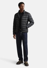 Fekete puffert dzseki vízszintes varrással, magas gallérral, teljes cipzárral és gumírozott mandzsettákkal. Fekete ing fölött viselve, sötét farmerrel és csizmával párosítva.