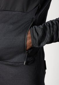 Pull en demi-zippé noir avec un tissu texturé, doté d'une poche sur le côté et de manches ajustées. Design épuré avec des motifs subtils.