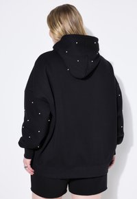 Sudadera negra con capucha, con detalles de perlas en las mangas y la parte trasera. Corte holgado con puños y dobladillo de canalé. Tejido simple y texturizado.