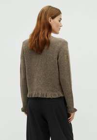 Barna gyapjú keverék pulóver rövidített fazonnal, rojtos szegéllyel és hosszú ujjal. A textúrás felület otthonos megjelenést biztosít.