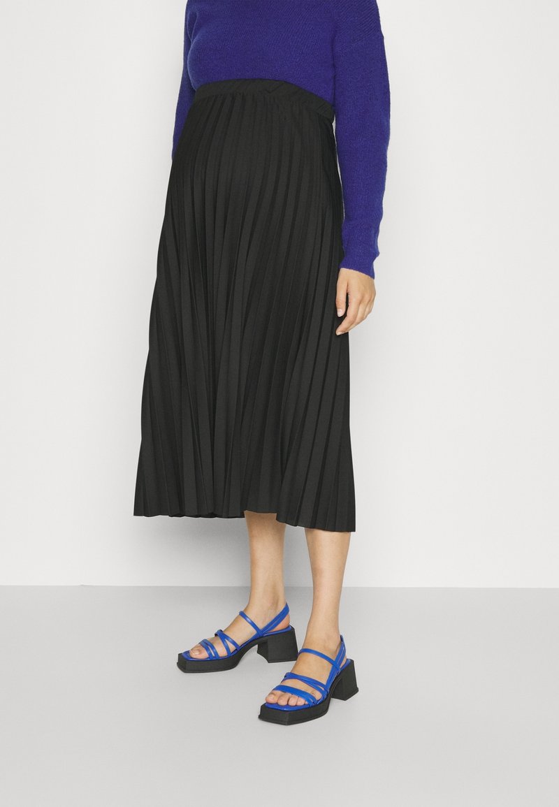 Gonna nera plissettata abbinata a un maglione blu e sandali blu con cinturini, dotati di un tacco nero spesso. Tessuto liscio e design fluido.