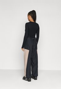 Cămășă neagră cu mâneci lungi, asortată cu pantaloni largi cu panouri bleumarin și bej. Materialul pare neted și ușor texturat.