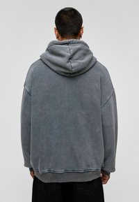 Overmaatse grijze hoodie met een gestructureerde afwerking, voorzien van een grote capuchon, verlaagde schouders en ribgebreide manchetten en onderkant.