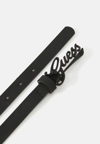 Zwarte leren riem met een glanzende zwarte metalen gesp waarop het "Guess" logo in cursieve lettertype staat. Gladde textuur, geen zichtbare patronen.