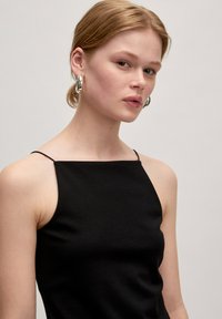 Schwarzes ärmelloses Top mit dünnen Trägern, aus glattem Stoff gefertigt, mit einer taillierten Passform und einem quadratischen Ausschnitt. Minimalistische Ästhetik.
