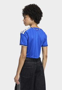 Blue, short-sleeve jersey with a leaf pattern, featuring gold-striped shoulder accents and a fitted design. Paired with black wide-leg pants.