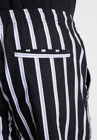 Czarno-białe szorty w paski z elastycznym pasem, wyposażone w tylną kieszeń obszytą białą lamówką. Gładka faktura materiału.