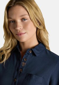 Marineblaues Poloshirt mit Knopfdetails und aufgesetzter Brusttasche. Verfügt über ein dezentes Markenlogo in der Nähe des Kragens und besteht aus strukturiertem Stoff.