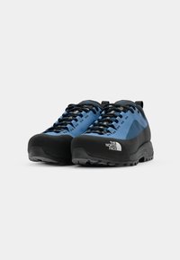 Blue and black trail shoes featuring a textured upper, rubber toe cap, durable laces, and a logo on the side; designed for outdoor use.