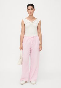 Top bianco con collo a cappuccio abbinato a pantaloni larghi in lino rosa chiaro. Gli accessori includono una piccola borsa bianca e sneakers bianche.