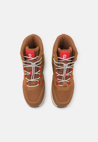 Zapatillas altas marrones con materiales de malla y ante, acentos rojos, cordones blancos y un cuello acolchado para mayor comodidad, con un cierre de tipo toggle.