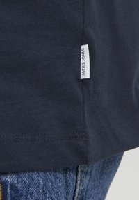 Marineblått bomulls t-skjorte med rett nederkant og korte ermer, med et hvitt stoffmerke sydd på den nedre siden med "JACK & JONES" tekst.