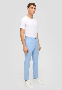 Hellblaue maßgeschneiderte Hose aus einem strukturierten Stoff, mit Gürtelschlaufen, Seitentaschen und schlanker Passform, kombiniert mit einem schlichten weißen T-Shirt und weißen Turnschuhen.
