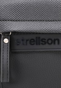 Borsa nera con una parte superiore in tessuto testurizzato e una sezione inferiore in pelle liscia. Include un logo in rilievo ben visibile e eleganti dettagli metallici.
