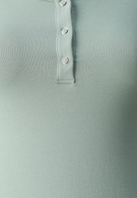 Mintgrønn ribbestrikket polo-skjorte med tre sølvfargede knappestøtter ved halslinjen, glatt tekstur og en figurtilpasset design.