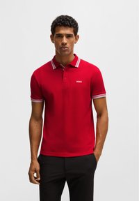 Rotes Poloshirt mit kontrastierendem gestreiftem Kragen und Ärmelb�ündchen, mit einem kleinen weißen Logo auf der Brust, aus einem glatten Stoff gefertigt.