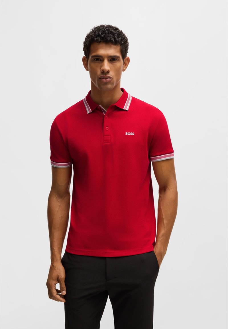 Rotes Poloshirt mit kontrastierendem gestreiftem Kragen und Ärmelbündchen, mit einem kleinen weißen Logo auf der Brust, aus einem glatten Stoff gefertigt.