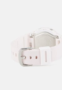 Montre blanche et rose avec un bracelet en silicone, boucle en métal argenté et un boîtier rectangulaire. Le dos présente des détails gravés.