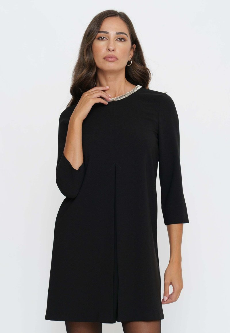 Schwarzes Shiftkleid mit Dreiviertelärmel, das einen runden Ausschnitt mit einer silbernen Perlenverzierung und einem geraden Schnitt aufweist.