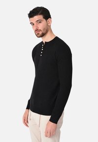 Maglione nero a maniche lunghe con scollo rotondo e patta con cinque bottoni, realizzato in tessuto testurizzato, silhouette aderente, polsini e orlo a costine.