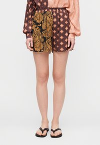 Σορτς με σχέδιο παϊέτας σε σκούρο καφέ και χρυσό, με ελαστική μέση και αντίθετο υφασμάτινο μοτίβο στη μία πλευρά. Μαύρες σαγιονάρες.