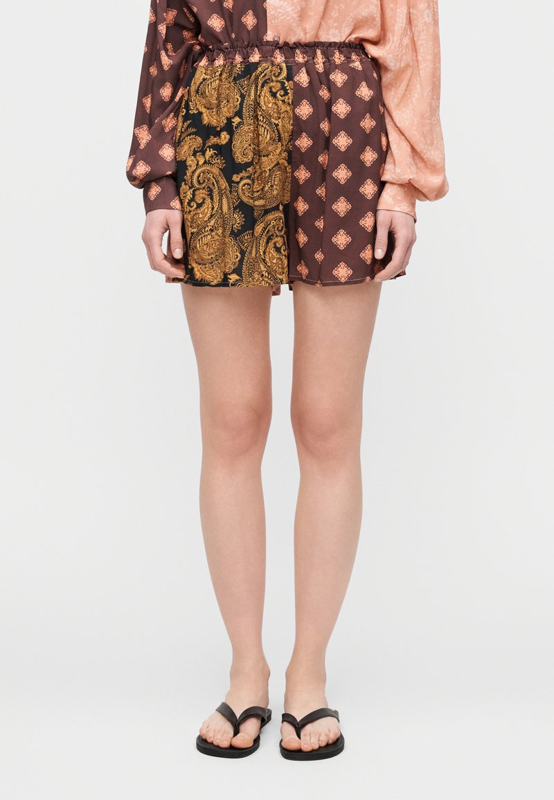 Σορτς με σχέδιο παϊέτας σε σκούρο καφέ και χρυσό, με ελαστική μέση και αντίθετο υφασμάτινο μοτίβο στη μία πλευρά. Μαύρες σαγιονάρες.