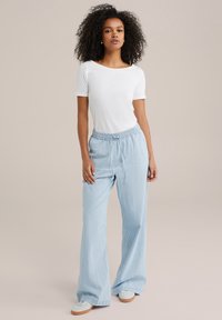 Pantaloni largi, cu dungi, de culoare albastru deschis, cu talie elastică și șnur. Asortați cu un tricou alb, ajustat, cu mânecă scurtă.