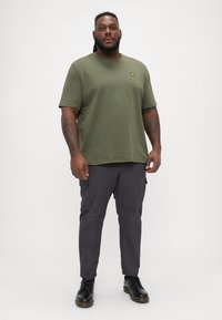 Tricou scurt de culoare verde măslin cu un logo galben, asortat cu pantaloni cargo gri. Ținuta are o croială relaxată și o textură fină.