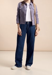 Ljuslila denimjacka över en vit T-shirt, parat med mörkblå vida jeans och vita sneakers. Inkluderar en vävd beige väska.