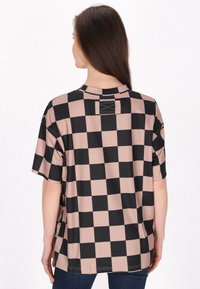 Camisa de manga corta con un patrón de cuadros en negro y rosa pálido, con un escote redondeado y un corte relajado. Textura de tela suave.