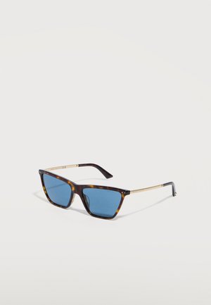 Lunettes de soleil rectangulaires en écaille de tortue avec verres bleus et fines branches dorées sur une surface blanche.