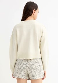 Suéter de punto color crema con un diseño corto, que presenta un escote redondeado y puños acanalados, combinado con pantalones cortos de tweed con estampado.