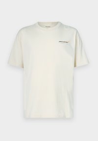 Bēša kokvilnas t-krekls ar īsām piedurknēm un apaļu apkakli. Kreisajā krūtīs neliels McLaren logotips oranžā un pelēkā krāsā.
