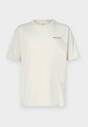 Beżowy bawełniany t-shirt z krótkimi rękawami i okrągłym dekoltem. Z przodu po lewej stronie mały logo McLaren w kolorze pomarańczowym i szarym.