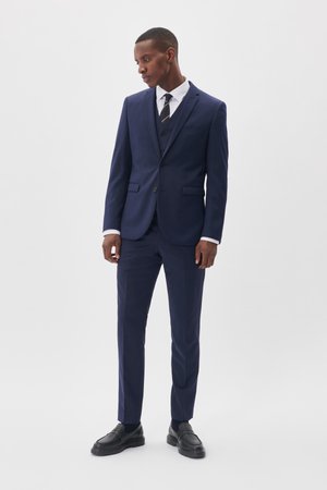 Marineblaues Anzug bestehend aus einem einreihigen Blazer mit Reverskragen, passender Hose, weißem Hemd und schwarzen Schuhen. Glatter Stoff, maßgeschneiderte Passform.