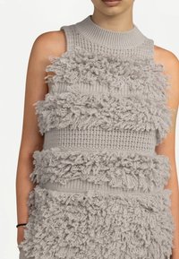 Haut sans manches en maille grise avec des rangées horizontales de détails en fil effiloché texturé sur la poitrine et le torse.