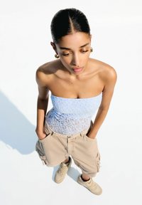 Svijetloplava čipkasta majica bez rukava, bež terenske šortse i bež visoke tenisice. Minimalistički dizajn s uskim siluetom i džepovima na šortsevima.