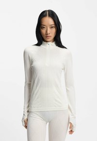 Biała bluzka z długim rękawem i wysokim kołnierzem, o fakturowanym splocie i dopasowanym kroju. Materiał zdobią subtelne diamentowe wzory oraz prążkowane ściągacze.
