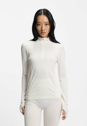 Biała bluzka z długim rękawem i wysokim kołnierzem, o fakturowanym splocie i dopasowanym kroju. Materiał zdobią subtelne diamentowe wzory oraz prążkowane ściągacze.