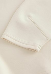 Short-sleeve garment in soft cream fabric, featuring a minimalist design with a clean hem and subtle stitching details.