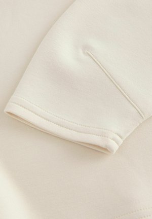 Îmbrăcăminte cu mânecă scurtă dintr-un material moale de crem, având un design minimalist cu un tiv curat și detalii de cusătură subtile.