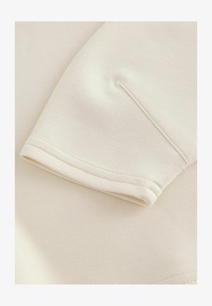 Trumpas rankovėmis drabužis iš minkštos grietinėlės spalvos medžiagos, turintis minimalistinį dizainą su švariu apdaila ir subtiliomis siuvinėjimo detalėmis.