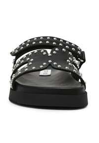 Sandales noires avec des accents cloutés, un design à large sangle, semelle plate, et matériau synthétique avec une surface texturée.