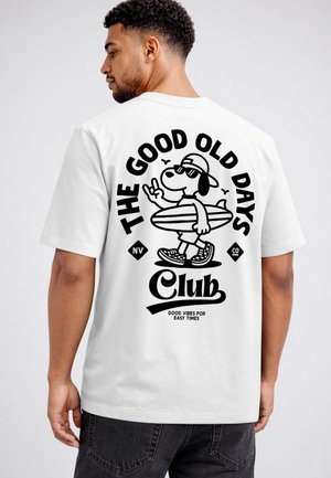 Man wearing white T-shirt showing back print of cartoon dog holding surfboard with "The Good Old Days Club" text.